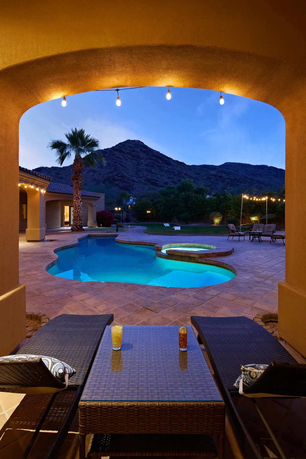 This exterior image showcases an elegant swimming pool area framed by a mountain backdrop, outdoor seating, and string lights. The tranquil scene hints at both relaxation and opportunities for group gatherings, perfectly reflecting the estate's upscale, resort-like amenities and serene Paradise Valley location.