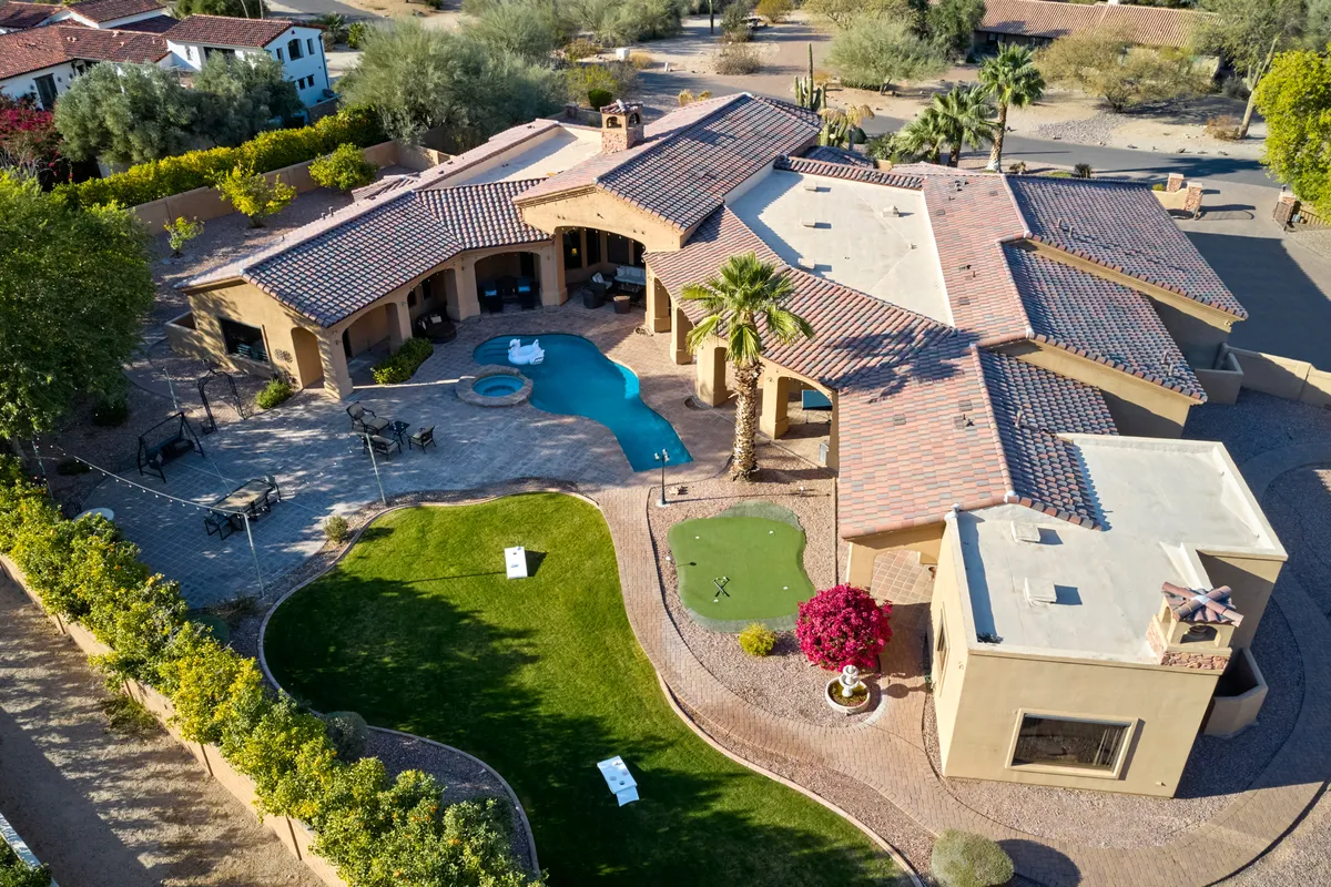 A vibrant exterior scene featuring a sparkling swimming pool in the foreground, a lush golf putting green, comfortable outdoor seating areas, and beautiful landscaping surrounding the space. The area is bathed in warm Arizona sunlight, showcasing inviting spaces for swimming, golf, and socializing.