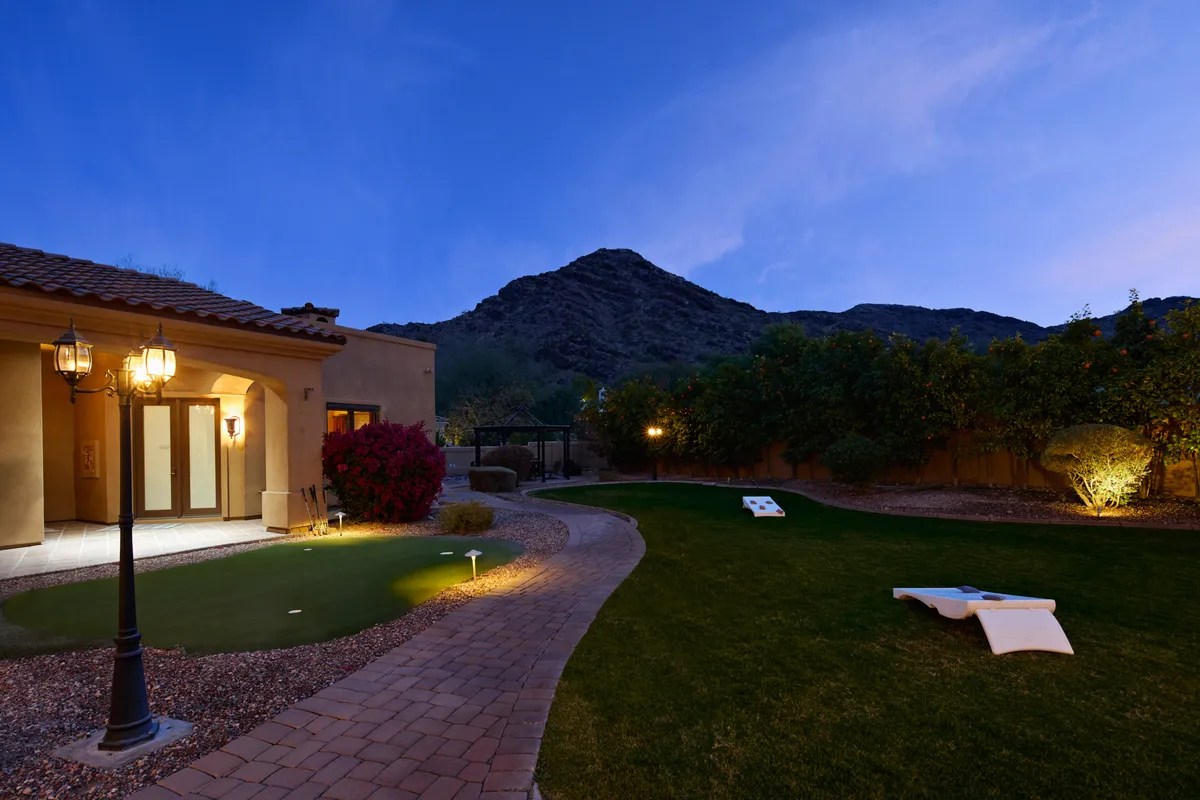 A fun and relaxed exterior setting with a mountain backdrop, manicured lawn, and an outdoor game set up for cornhole. Subtle lighting enhances the evening mood, and the mountains frame the scene, inviting guests to play and unwind as the sun sets.