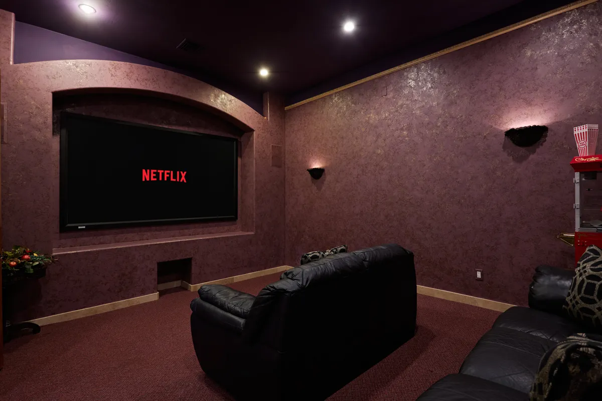 This image features a private theater room with large, comfortable seating arranged to face a big screen displaying the 'NETFLIX' logo. A popcorn machine stands nearby, adding a playful, cinematic touch. The lighting is low and cozy, enhancing the ambiance of a home theater experience.