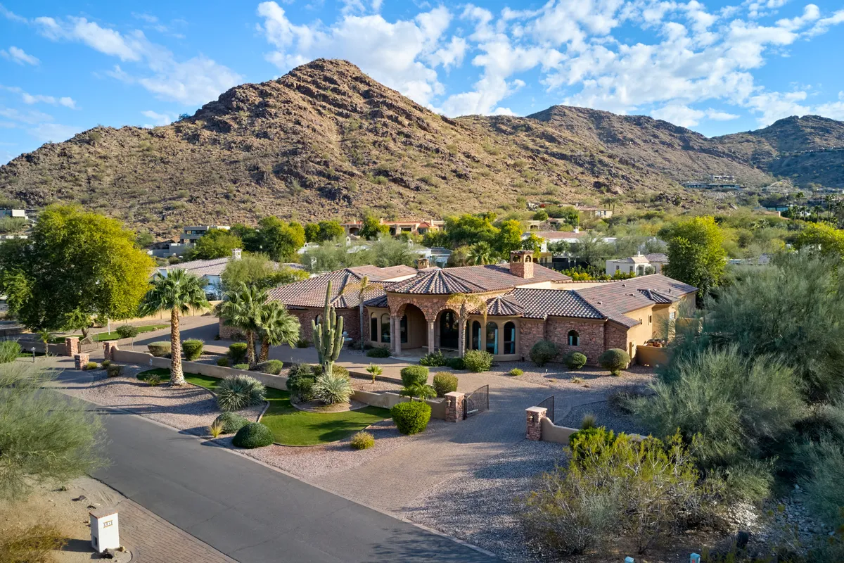 The image showcases an elegant single-family estate nestled against a stunning mountain backdrop, with a spacious driveway flanked by lush landscaping and rich architectural details. The scene exudes tranquility, inviting guests to imagine outdoor gatherings, relaxing in the garden, or savoring the sweeping natural views.