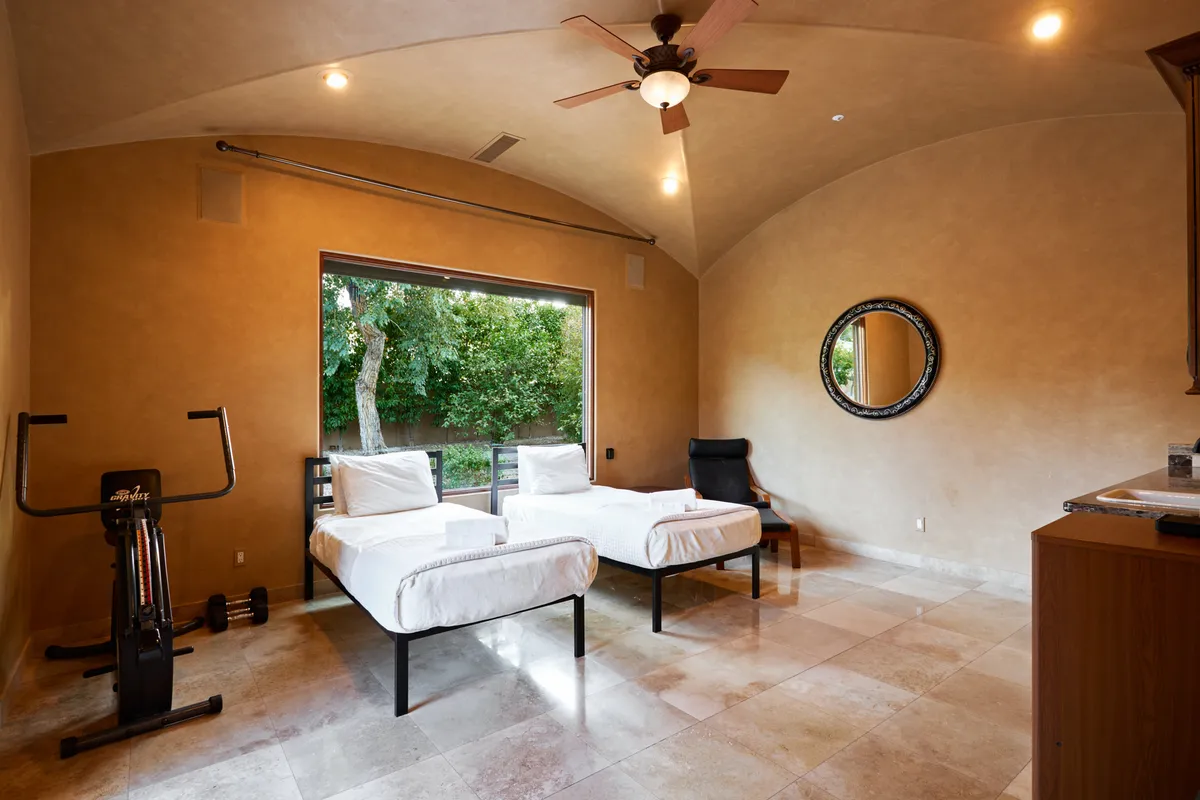 This image features a bonus room with two twin beds, a large window with a scenic view, exercise equipment, and a mirror. The room feels open, tranquil, and versatile—well-suited for families or extra guests.