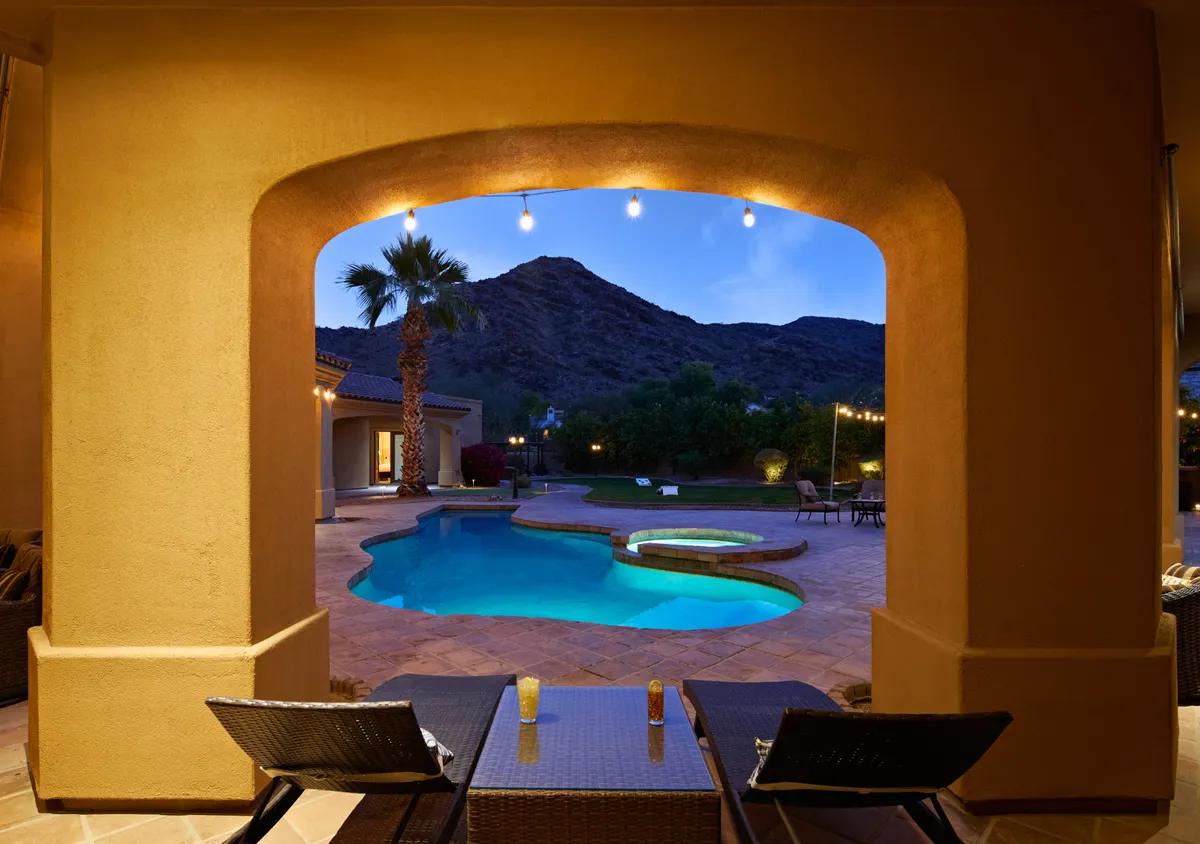 A serene mountain backdrop frames the shimmering pool and spacious outdoor seating, all set beneath a sky transitioning to evening. String lights and tasteful landscaping invite guests to relax or celebrate, with the estate’s privacy and scenic beauty on display.