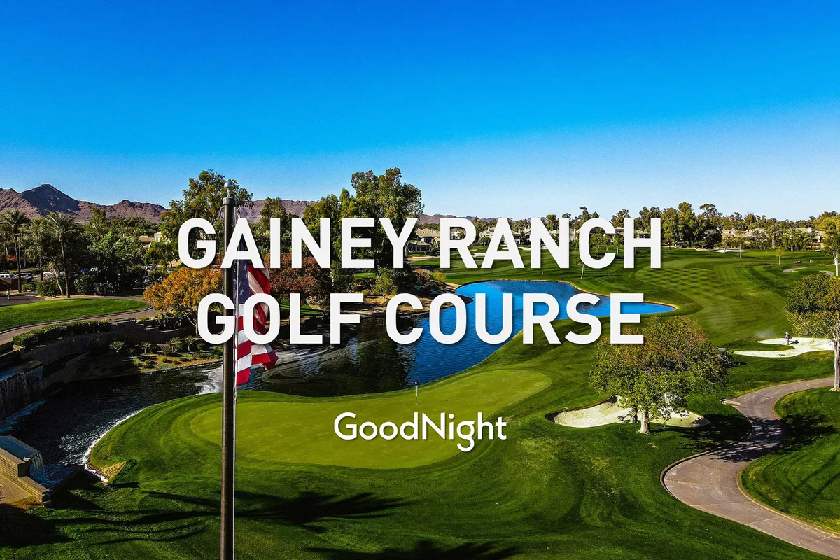 A serene view of a lush golf course bordered by a pond, with mountains and trees in the background. A flag on the green signals an active course, while the calm water and natural surroundings invite relaxation and outdoor enjoyment.