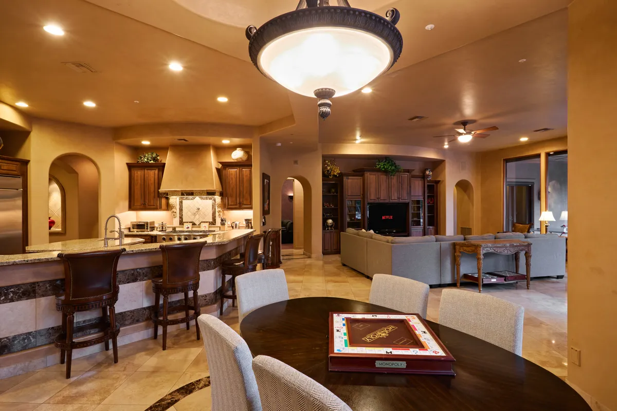 A wide-angle shot of the home's core gathering area, featuring a kitchen island, adjacent dining table, and a comfortable living space. The image captures the fluid transition between cooking, dining, and lounging, with elegant finishes and a welcoming atmosphere.