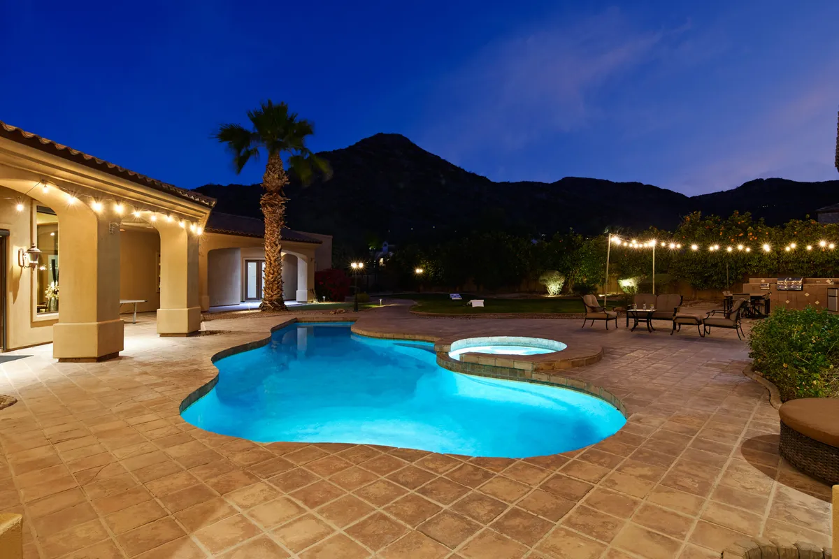A stylish outdoor living area with a pool, hot tub, mountain views, and warm string lights overhead. The setting exudes relaxed luxury—ideal for post-golf unwinding, socializing, or enjoying a celebratory evening meal with friends.