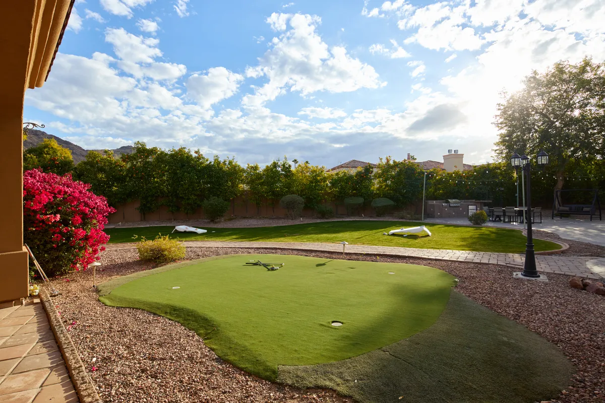 A beautifully landscaped outdoor area featuring a putting green, colorful flowers, a manicured lawn, and a cozy seating area. The space is ideal for gathering, playing games, and enjoying meals or conversations in a garden setting.